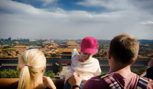 Smiling family with children exploring a traditional Chinese garden with red lanterns and pagodas.