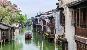 Peaceful view of West Lake in Hangzhou with a traditional boat and weeping willow trees along the shore.
