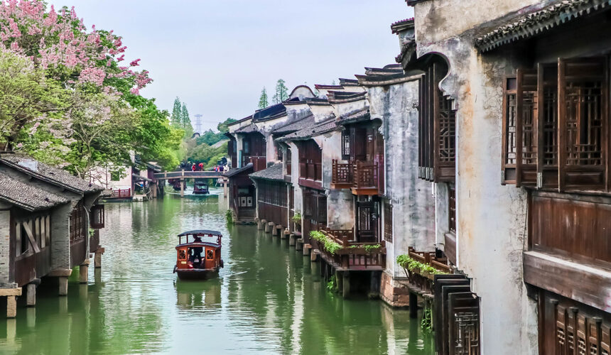 Peaceful view of West Lake in Hangzhou with a traditional boat and weeping willow trees along the shore.