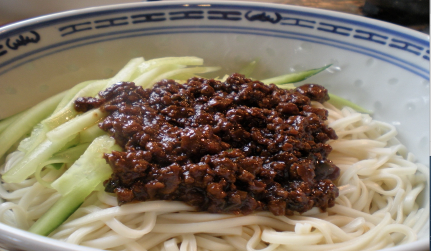 Bowl of Beijing zhajiangmian noodles topped with savory soybean paste and fresh vegetables.