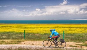 Cyclist riding along a scenic path beside Qinghai Lake under a blue sky
