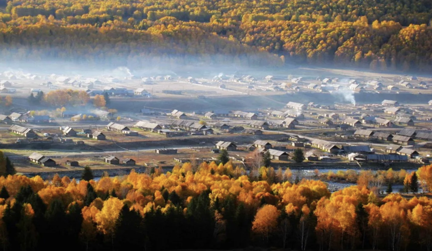 Rustic wooden cabins and snowcapped mountains surrounding Hemu Village in Xinjiang.