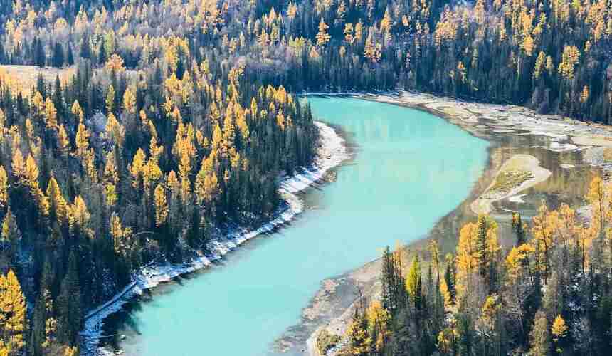 Tranquil turquoise waters of Kanas Lake surrounded by dense forests and snow-capped peaks in Xinjiang