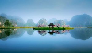 Tranquil lake surrounded by green hills and lotus flowers at Puzhehei Scenic Resort in Yunnan.
