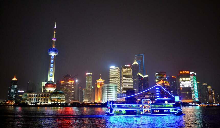 Nighttime river cruise boat on the Huangpu River with illuminated skyline in the background.