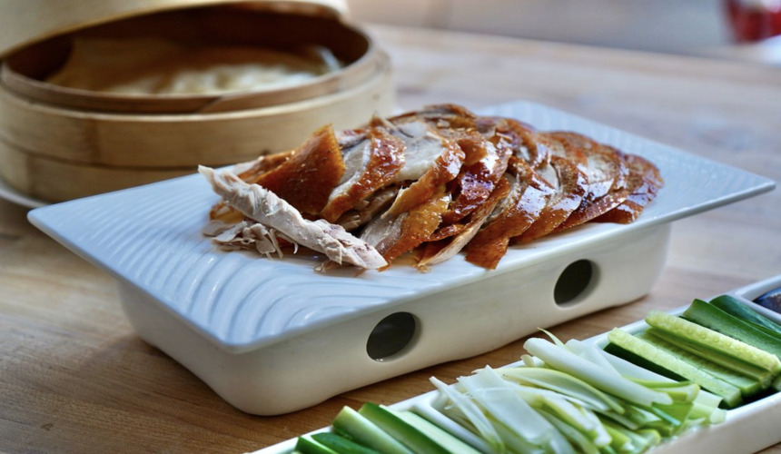 Crispy sliced Peking duck served with pancakes, scallions, and hoisin sauce on a wooden platter.