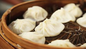 Close-up of steaming Shanghai xiao long bao soup dumplings in a bamboo steamer.