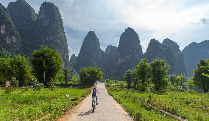 Tourist cycling along a rural path in Yangshuo with scenic mountain views.