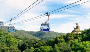 Cable cars of Ngong Ping 360 gliding over lush green mountains with the Big Buddha in the distance.