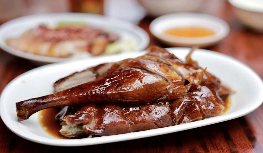 Plate of juicy Hong Kong roast goose with crispy skin and plum sauce.