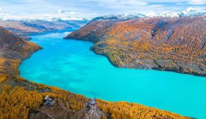 Crystal-clear Kanas Lake in Xinjiang surrounded by autumn-colored forests and mountain reflections.