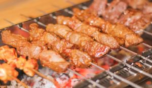 Chinese barbecue alley at night with street vendors grilling skewers and diners eating outdoors.