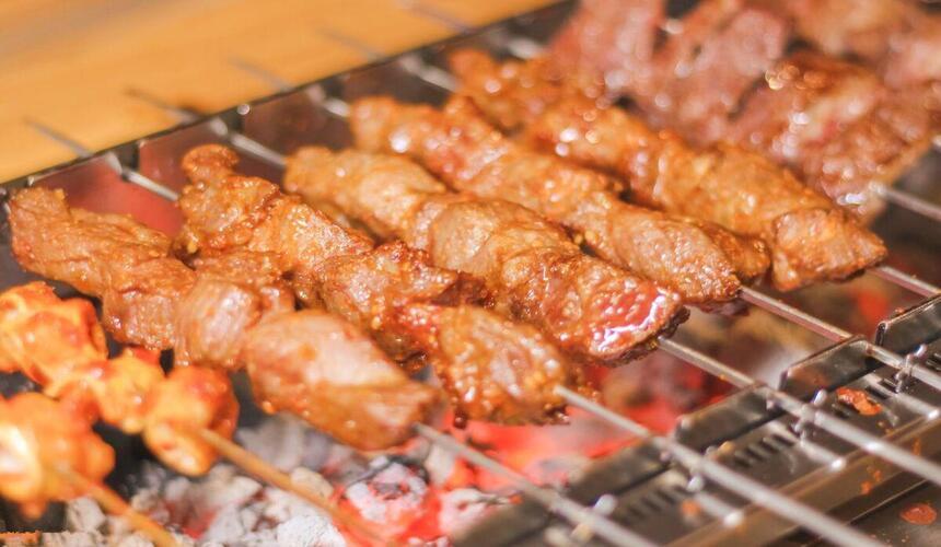 Chinese barbecue alley at night with street vendors grilling skewers and diners eating outdoors.