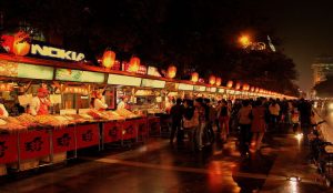 Night market in China with food stalls, bright lights, and claw machine arcades.