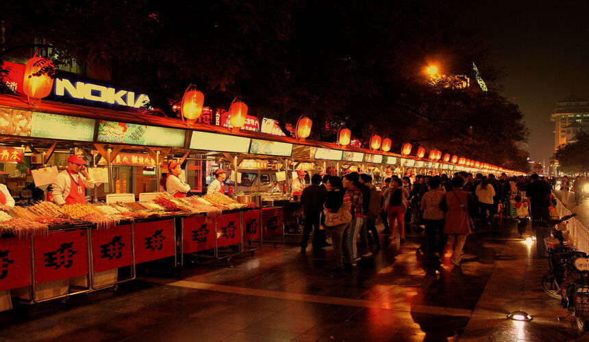 Night market in China with food stalls, bright lights, and claw machine arcades.
