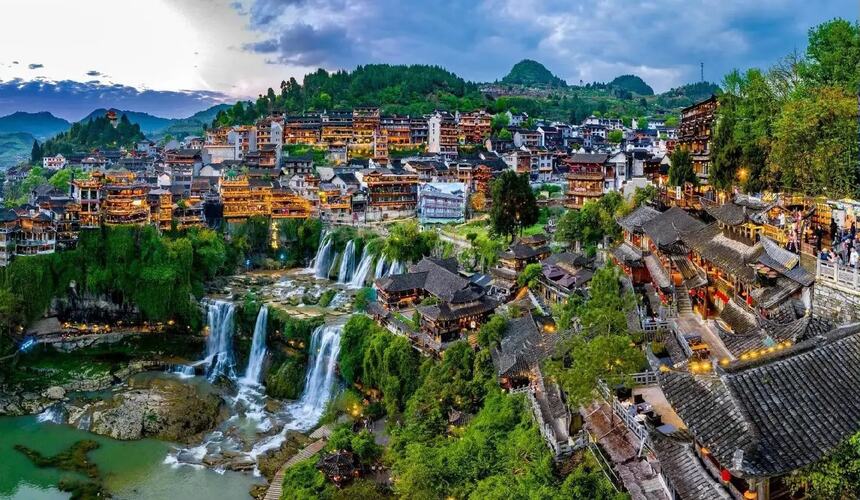 Waterfall flowing through Furong Ancient Town with historic buildings perched above in Zhangjiajie