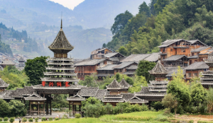 Traditional Dong wooden houses and drum towers surrounded by green mountains in Zhaoxing Dong Village, Guizhou, China.