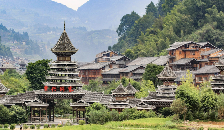Traditional Dong wooden houses and drum towers surrounded by green mountains in Zhaoxing Dong Village, Guizhou, China.
